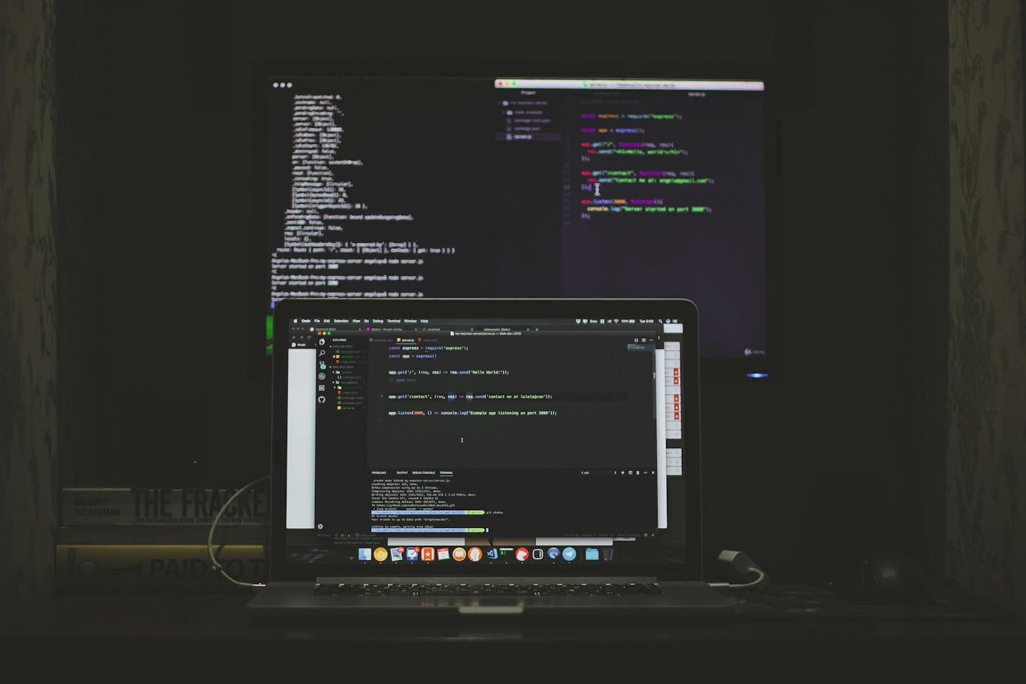 Laptop en externe monitor met code op een bureau.